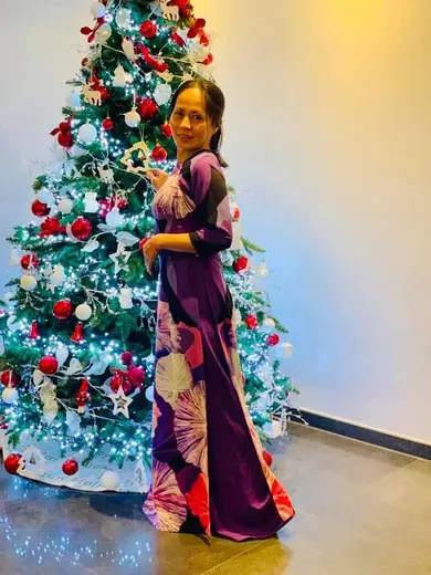 Một phụ nữ mặc áo dài tím in hình lá đứng bên cây thông Noel.
