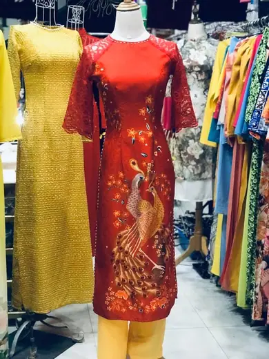Áo dài đỏ in chim phượng tay lỡ cạnh áo dài ren vàng trên ma-nơ-canh.