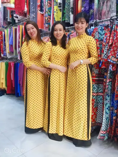 Ba phụ nữ mặc áo dài đồng phục vàng chấm bi đen đứng trong tiệm.