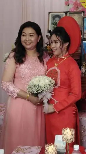 Một phụ nữ mặc áo dài hồng đính ren chụp cùng cô dâu mặc áo dài đỏ đội mấn.