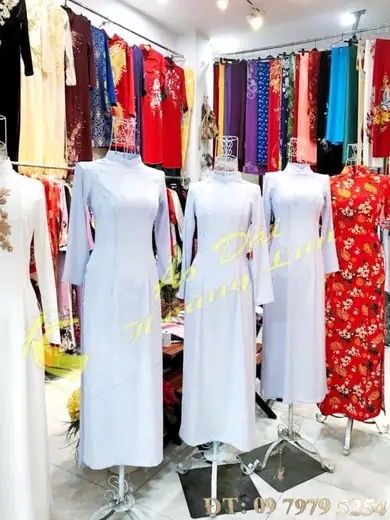 Ba chiếc áo dài trắng nữ sinh trên ma-nơ-canh trong tiệm, ảnh có logo tiệm.