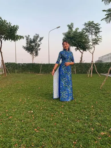Một phụ nữ mặc áo dài xanh hoạ tiết đứng trên bãi cỏ.