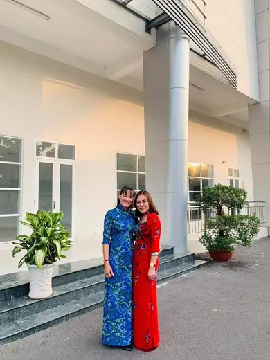 Hai phụ nữ mặc áo dài xanh và đỏ đứng trước toà nhà.