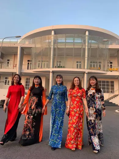 Năm phụ nữ mặc áo dài nhiều màu bước đi trước nhà thi đấu.