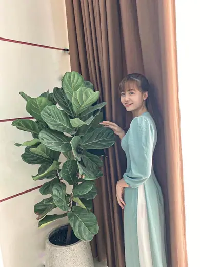 Một cô gái mặc áo dài xanh bạc hà tay phồng đứng bên chậu cây.