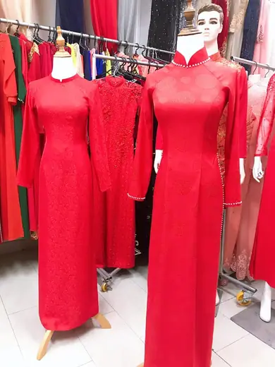 Hai chiếc áo dài cưới đỏ bằng gấm và ren trên ma-nơ-canh.