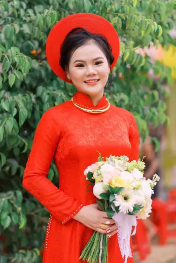 Chân dung cô dâu mặc áo dài ren đỏ, đội mấn, ôm bó hoa trắng.
