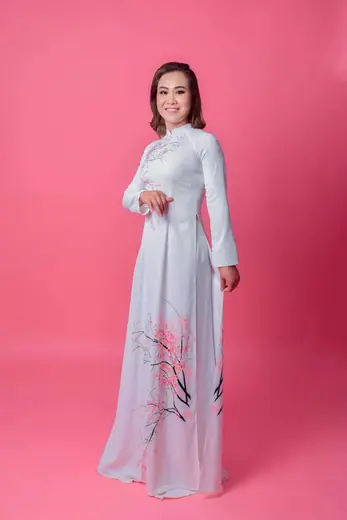 Một phụ nữ mặc áo dài xám nhạt vẽ hoa sen, chụp trên nền hồng.