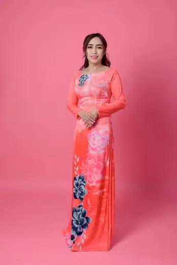 Một phụ nữ mặc áo dài hồng san hô in hoa sen xanh, toàn thân.