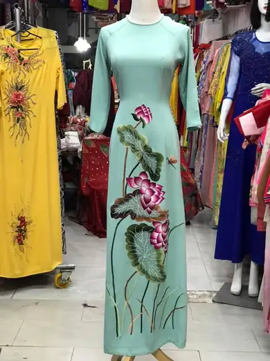 Áo dài xanh bạc hà thêu hoa sen cạnh áo dài vàng thêu hoa trên ma-nơ-canh.
