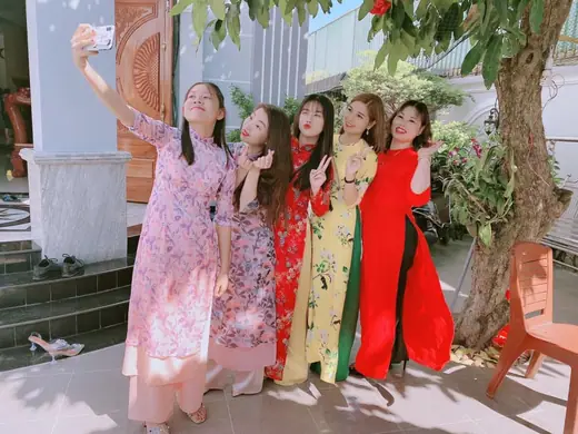 Bốn phụ nữ mặc áo dài nhiều màu cùng chụp ảnh tự sướng trước sân nhà.