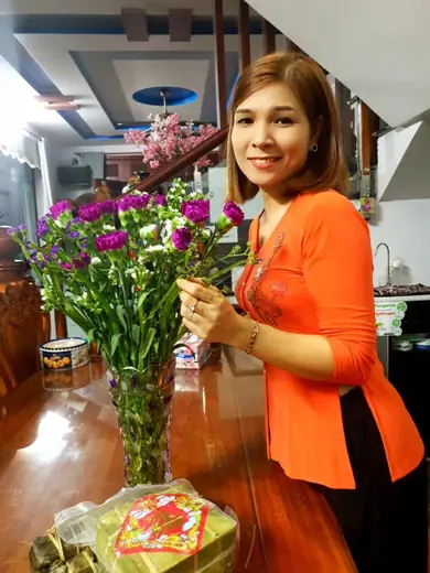 Một phụ nữ mặc áo cam cắm hoa trong nhà.