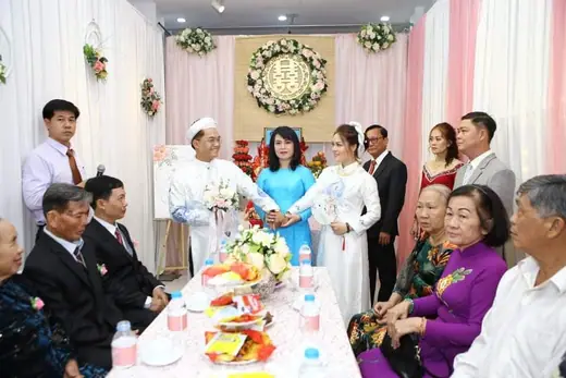 Cô dâu chú rể mặc áo dài trắng rót trà mời họ hàng trong lễ gia tiên.