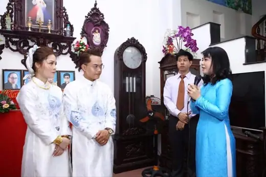Lễ gia tiên trong nhà, cô dâu chú rể mặc áo dài trắng đứng trước bàn thờ.