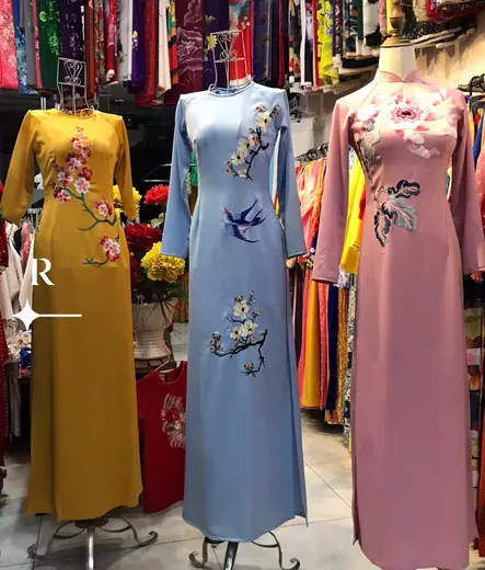 Ba chiếc áo dài thêu hoa và chim én trên ma-nơ-canh trong tiệm.