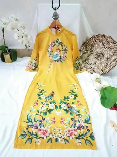 Áo dài cách tân vàng vẽ hoa và chim, trải phẳng bên đồ trang trí.