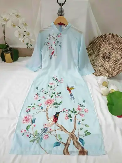 Áo dài cách tân xanh nhạt vẽ cành hoa và chim, trải phẳng.