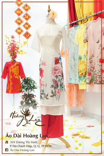 Áo dài cách tân trắng vẽ hoa phối quần đỏ và áo trẻ em đỏ trên ma-nơ-canh, khung ảnh có tên và địa chỉ tiệm.