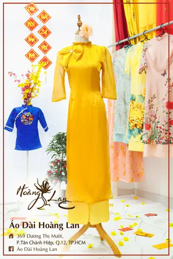 Áo dài cách tân vàng cổ thắt nơ và áo trẻ em xanh dương, khung ảnh có tên tiệm.