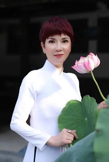 Một phụ nữ mặc áo dài trắng cầm bông sen trên nền tối.