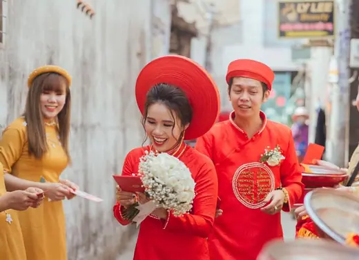 Cô dâu chú rể mặc áo dài đỏ, đội mấn, cùng một phụ nữ mặc áo dài vàng trong ngày cưới.