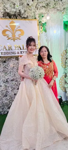 Một phụ nữ mặc áo dài đỏ chụp cùng cô dâu mặc váy cưới tại sảnh tiệc.