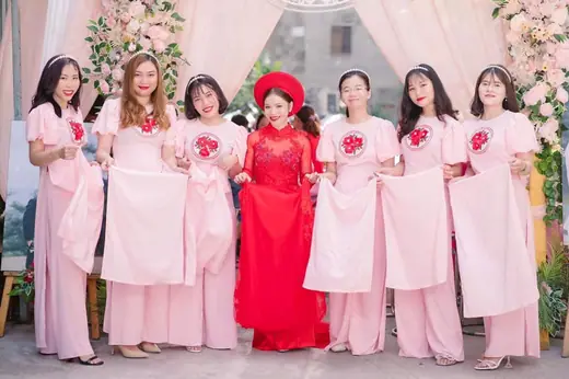 Cô dâu mặc áo dài đỏ đứng giữa dàn phù dâu mặc áo dài hồng.