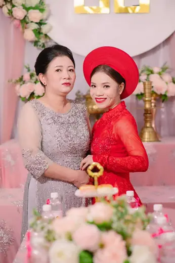 Cô dâu mặc áo dài ren đỏ, đội mấn, bên mẹ mặc đầm xám kết cườm.