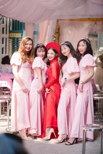 Cô dâu mặc áo dài đỏ cùng các phù dâu áo hồng đứng trước rạp cưới.