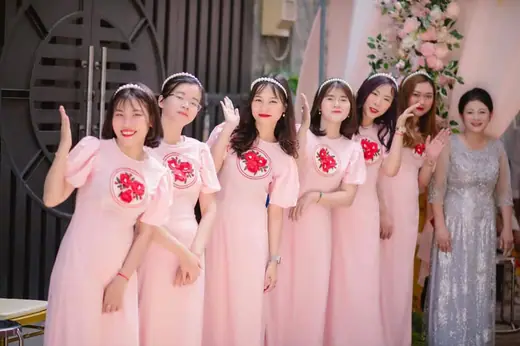 Dàn phù dâu mặc áo dài hồng đính hoa đỏ đứng thành hàng.