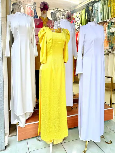 Ba chiếc áo dài trắng và vàng tay bồng trên ma-nơ-canh trong tiệm.