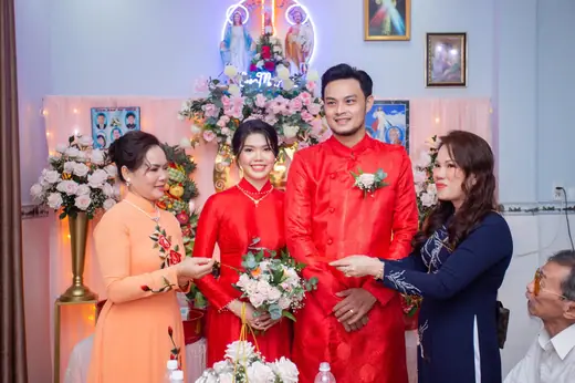 Cô dâu chú rể mặc áo dài đỏ cùng hai bà mẹ trước bàn thờ trong lễ gia tiên.