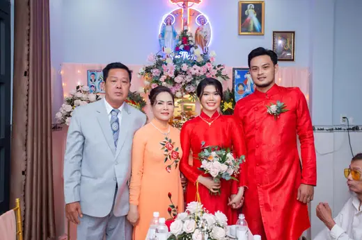 Cô dâu chú rể mặc áo dài đỏ chụp cùng cha mẹ, người mẹ mặc áo dài cam thêu hoa.