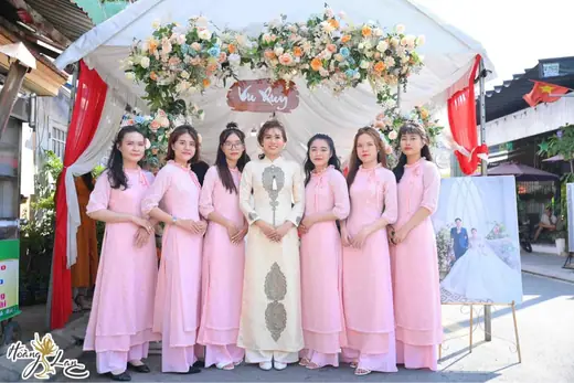 Cô dâu và dàn phù dâu mặc áo dài hồng trước cổng hoa đám cưới.