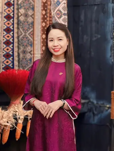 Một phụ nữ mặc áo dài tím hồng tay rộng đứng trong quán trang trí Tết.