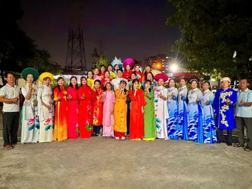 Đội thi đông người mặc áo dài nhiều màu chụp chung ngoài trời buổi tối.